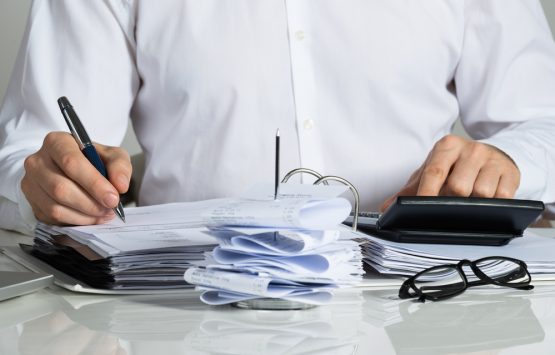 Midsection of businessman calculating invoice at office desk